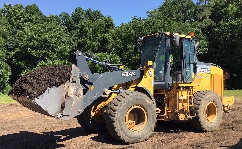 City staff operating earth mover to move large pile of compost