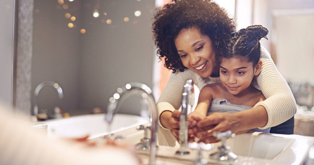 woman with daughter washing hands in bathroom sink